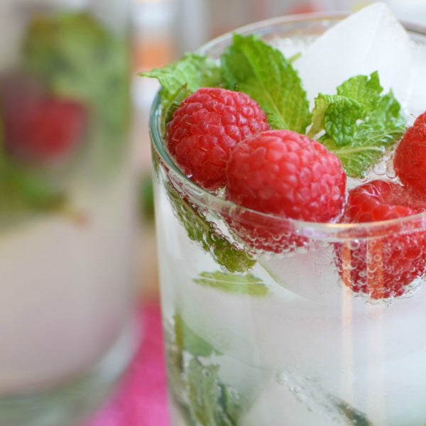 Closeup of glass with mocktail, showing rasberry and mint garnish.